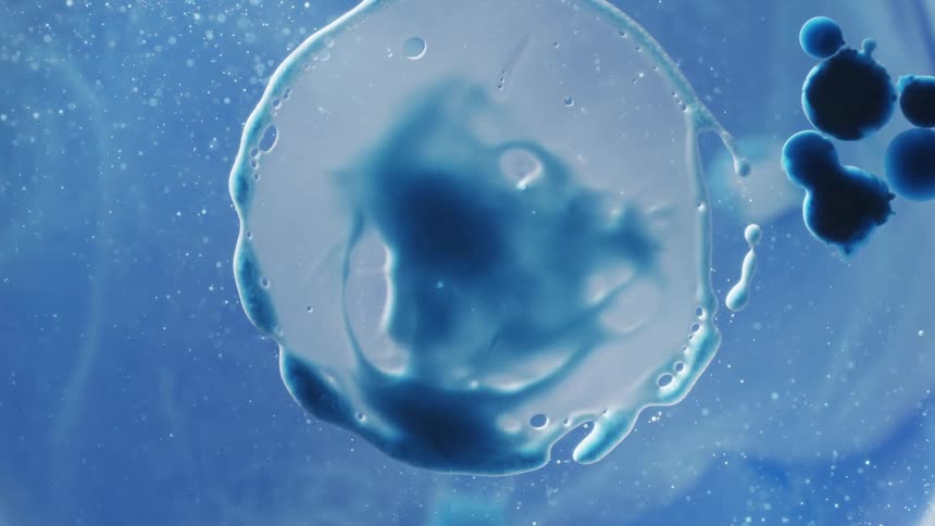 Close up of a bubble of blue flowing liquid ink forming over a translucent surface