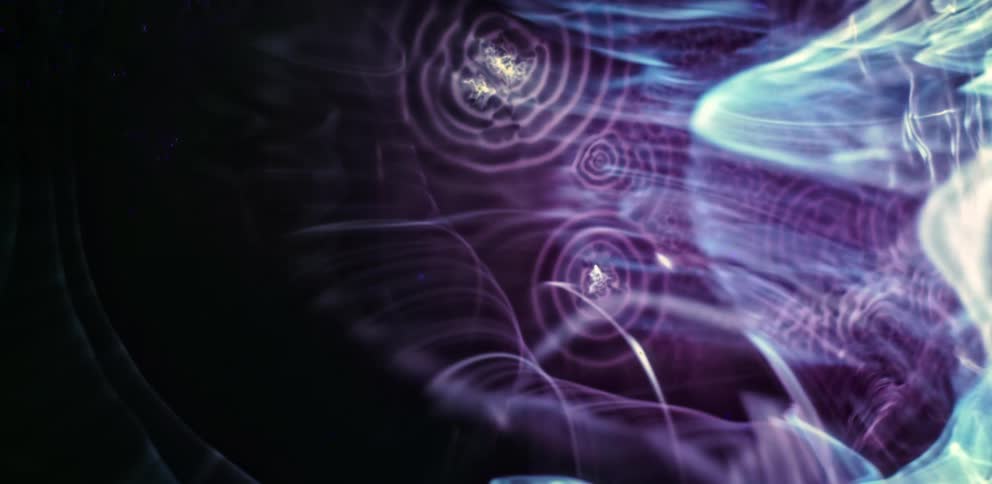 Strands and wisps of purple and blue colors floating against a black background
