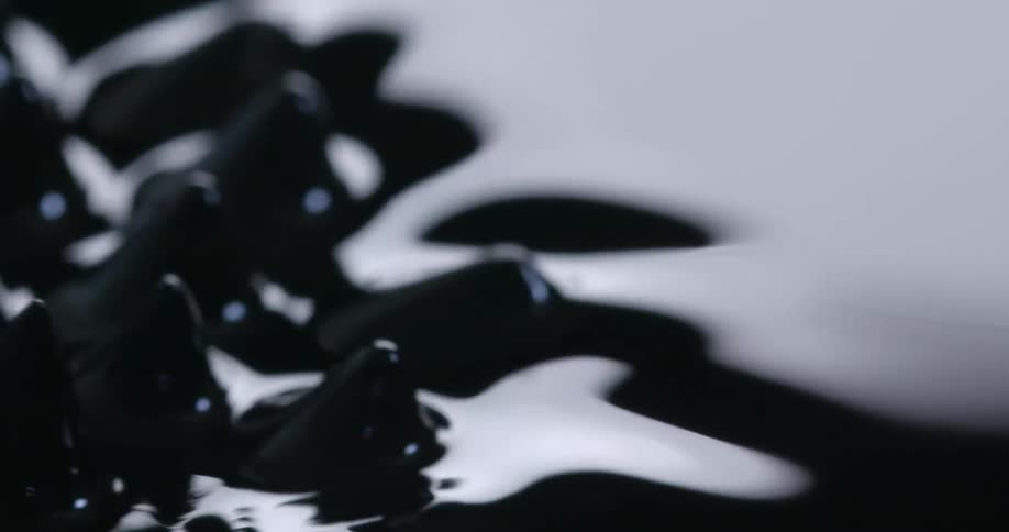 Close up of spikes protruding from the surface of a bright black liquid