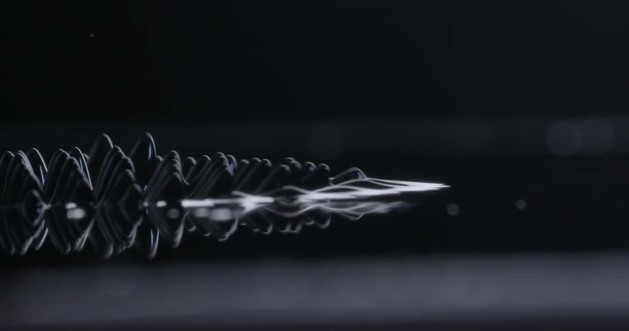 White outlined dark shape with multiple peaks moves wave like across dark surface