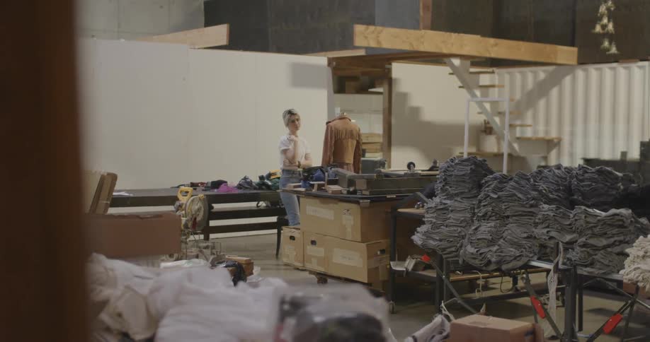 A woman adjusts a brown jacket on a stand