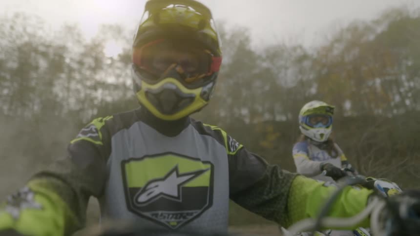 Motorcycle riders sit on motorcycles in foggy forest wearing helmets and racing suits
