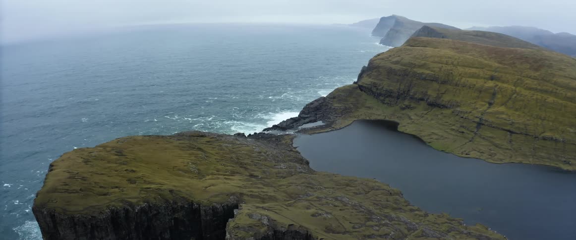 An aerial view of a cliff on the shore with water flowing to the ocean below