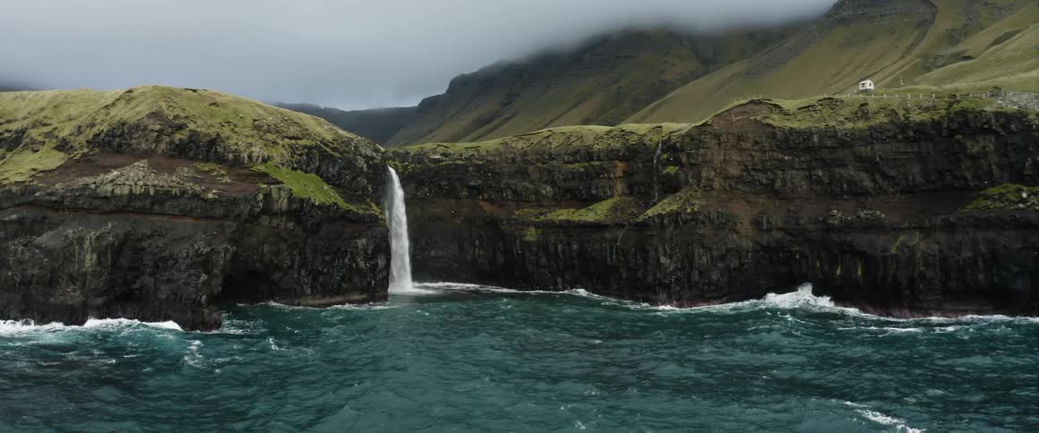 A waterfall gushing over the side of a coastal cliff into the sea