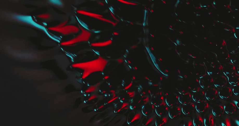 Top down view of spikes growing out of a black liquid reflecting red and blue lights