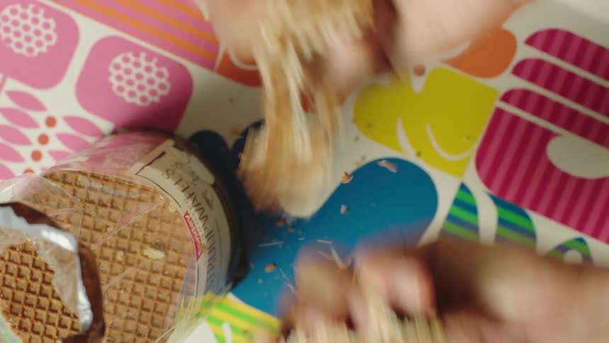 A person breaking a wafer in two over a colorful tablecloth
