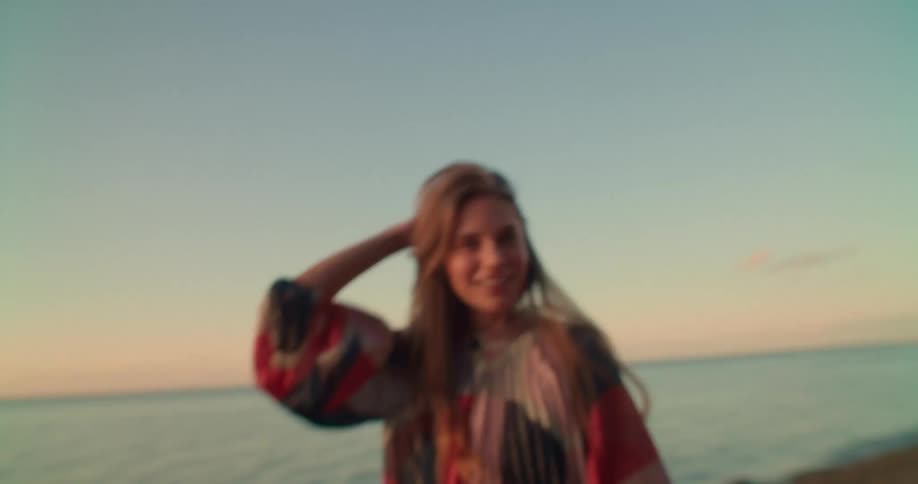 A woman is standing outdoors at the beach while the sun is setting