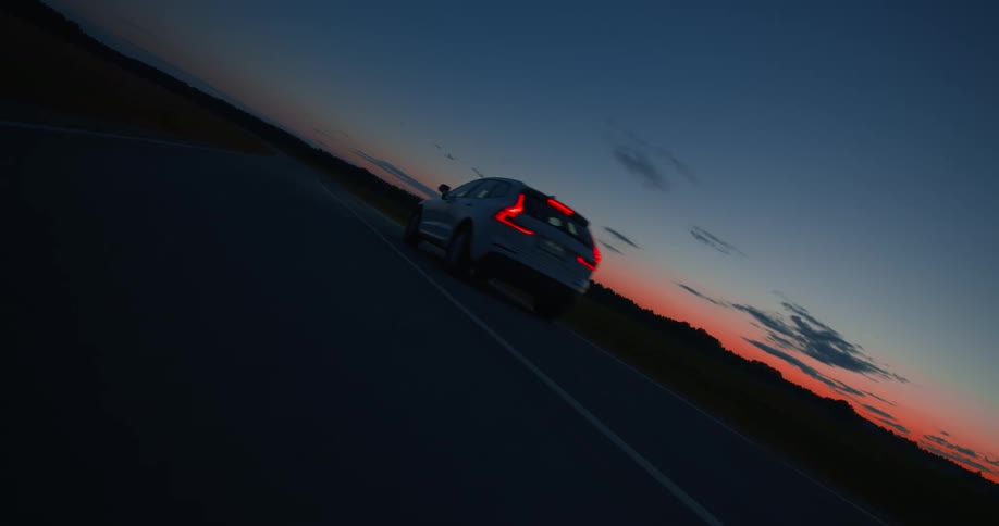 A white car traveling on a rural road at sunset