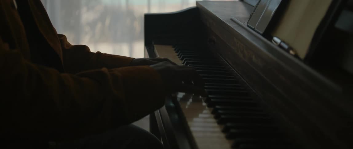 A man is sitting indoors and playing the piano