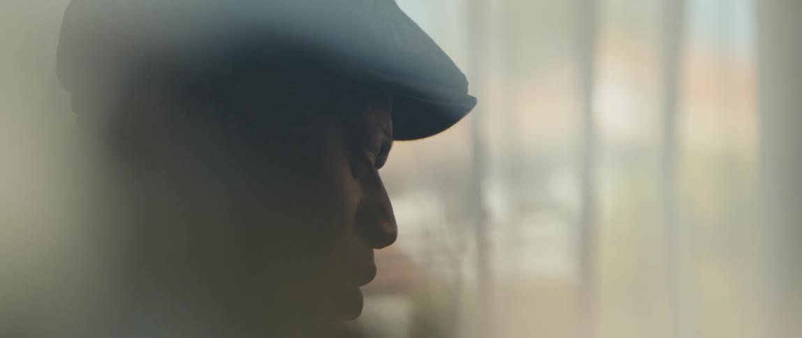 A man singing and playing piano in front of a curtained window