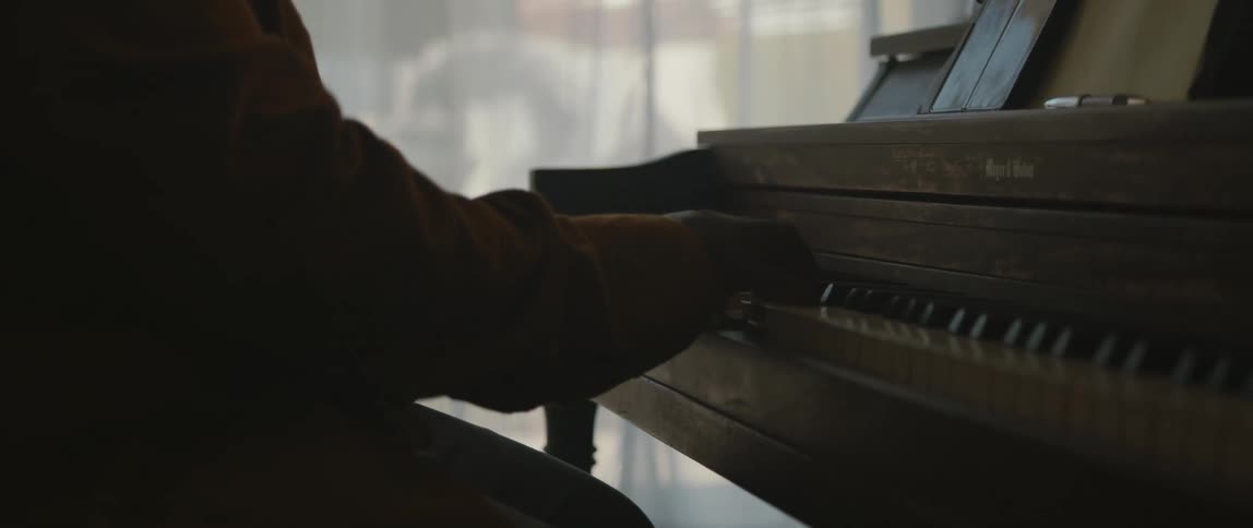 A person playing a piano in front of a curtained window