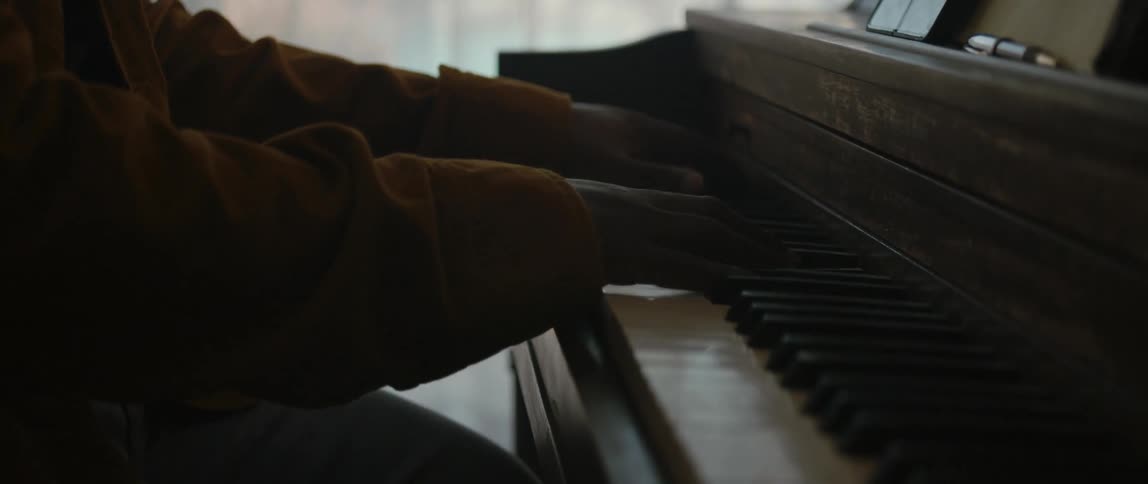 Male pianist with black cap and orange jacket plays piano in room