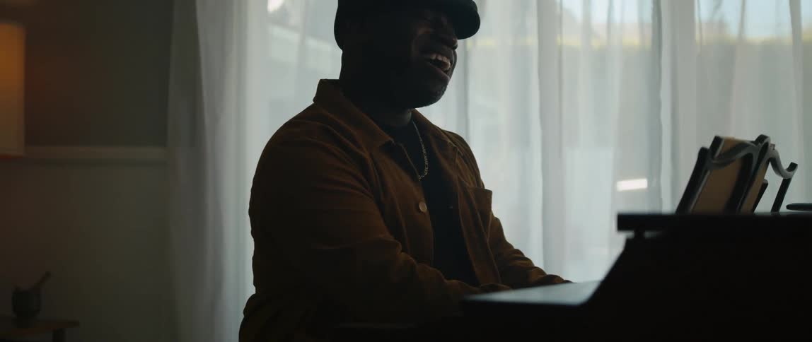 A young black man is playing the piano in the living room