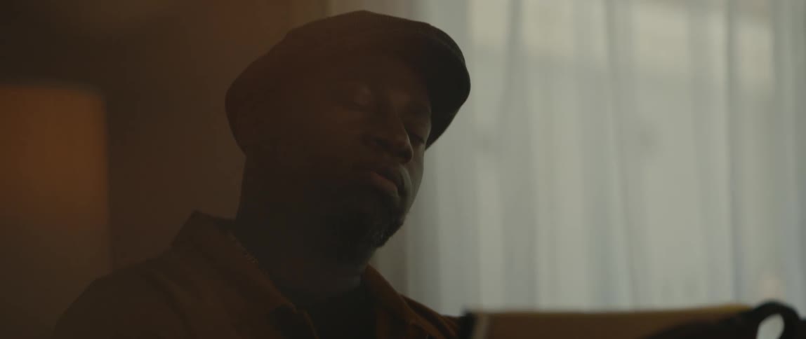 Male musician with black cap and orange jacket plays piano in room