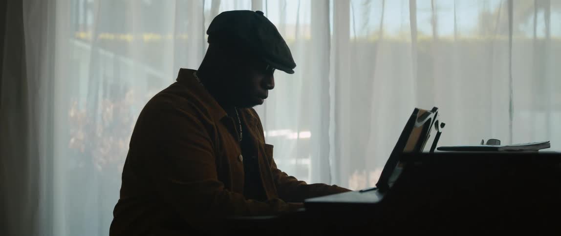 A man is sitting near a window and playing the piano