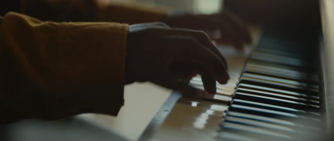 Male pianist with black cap and orange jacket plays piano in room