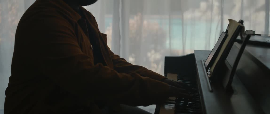 A man is sitting near a window and playing the piano