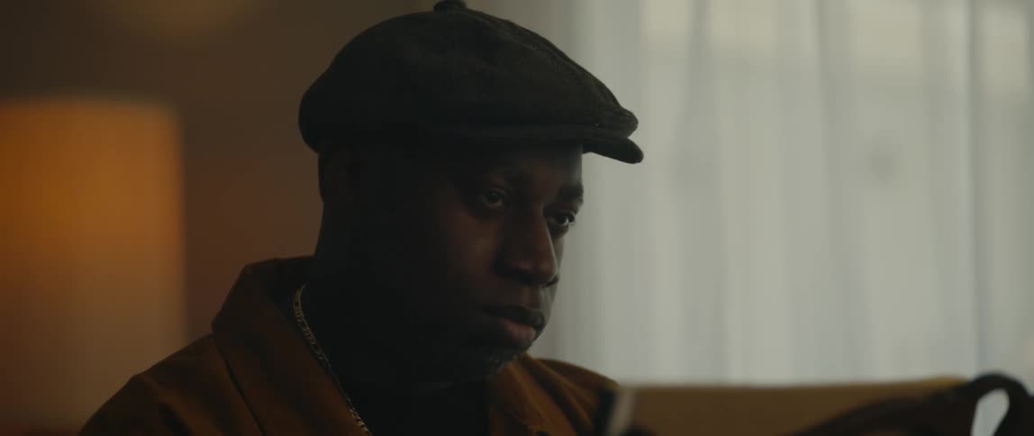 A black man is wearing a hat and sitting down