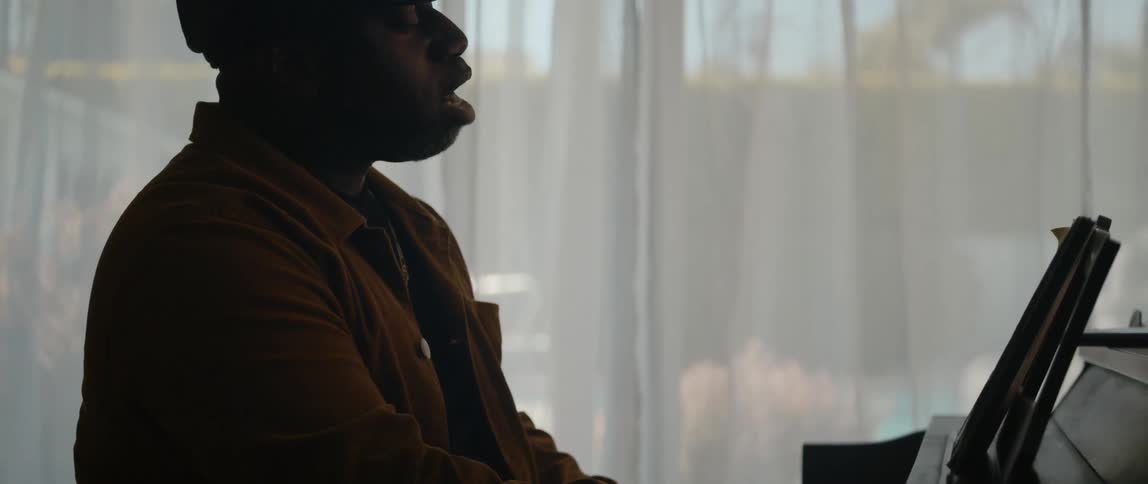 A man singing and playing piano in front of a curtained window