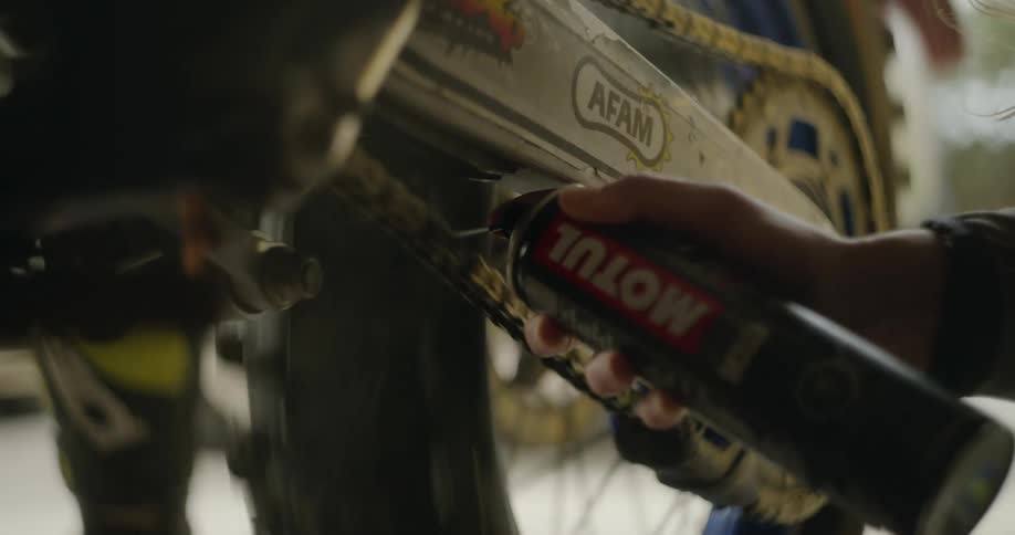 A person sprays lubricant on the dirt bike chain