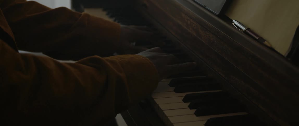 Male pianist with black cap and orange jacket plays piano in room