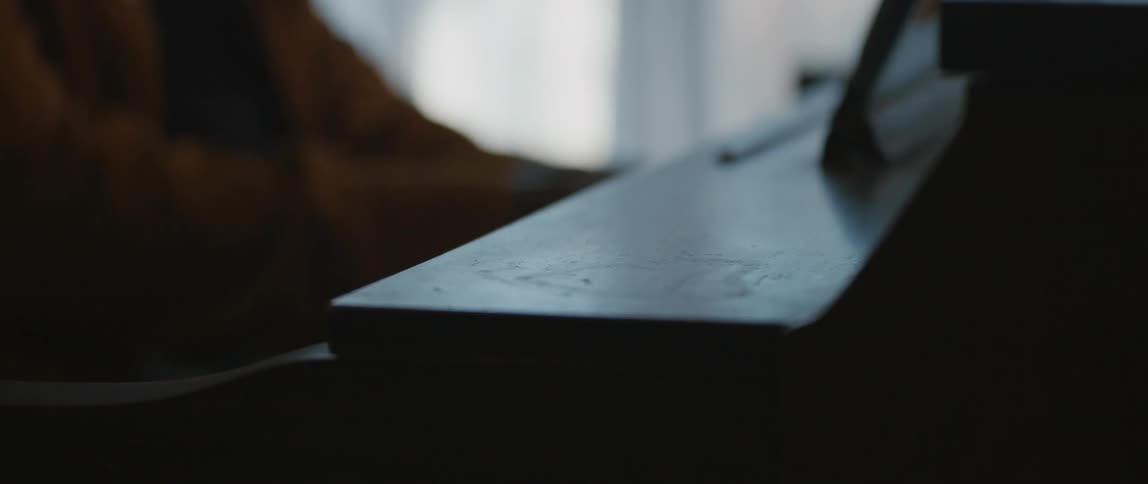 Male pianist with black cap and orange jacket plays piano in room