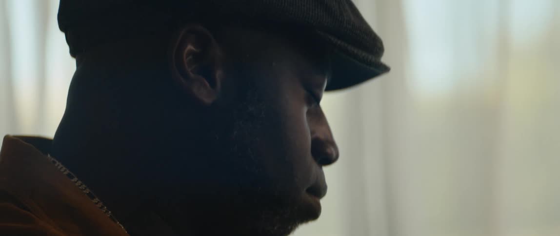 A man is sitting indoors and wearing a hat