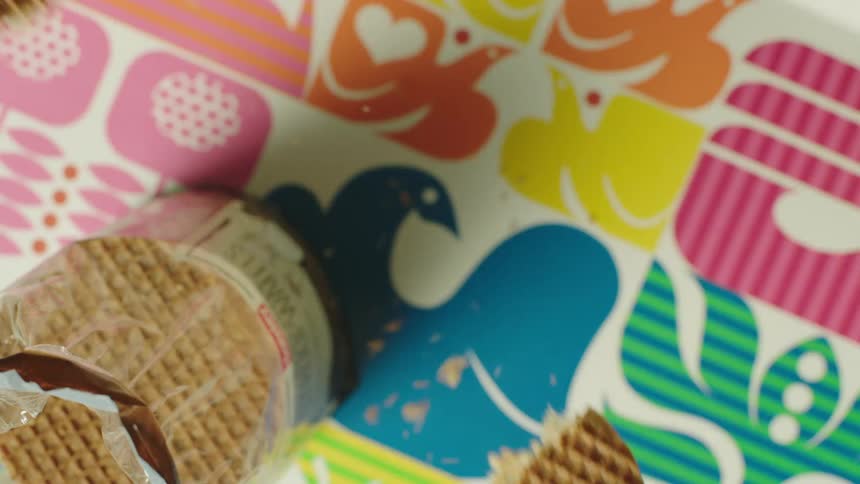 A person snapping a wafer in two over a colorful tablecloth