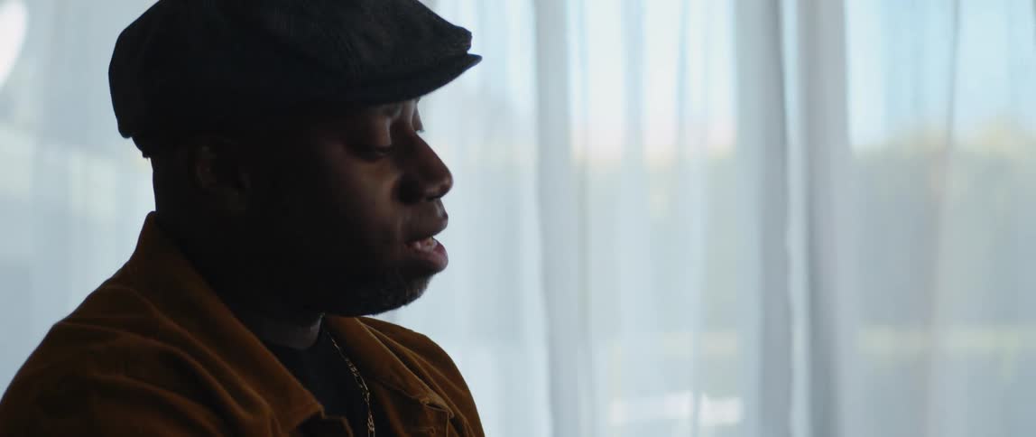 A man singing and playing piano in front of a curtained window