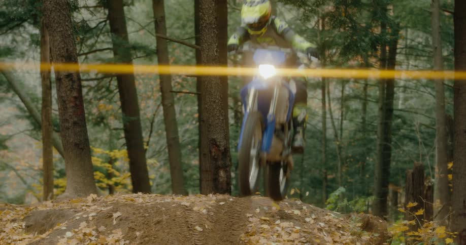 A teenager on a motorbike leaps over an embankment in the woods