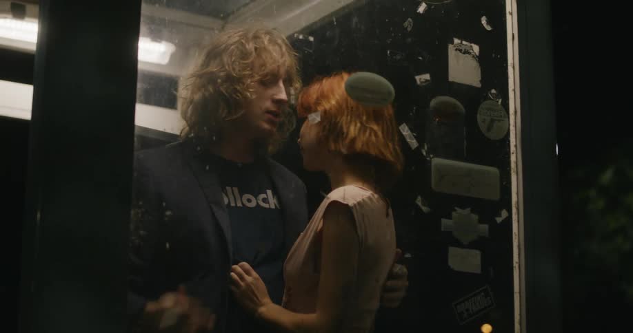A young man lights a cigarette as a woman is hugging and touching him