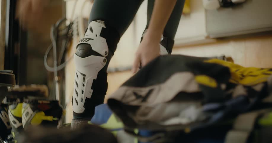 Woman puts on knee protection before picking up racing suit pants as another person watches