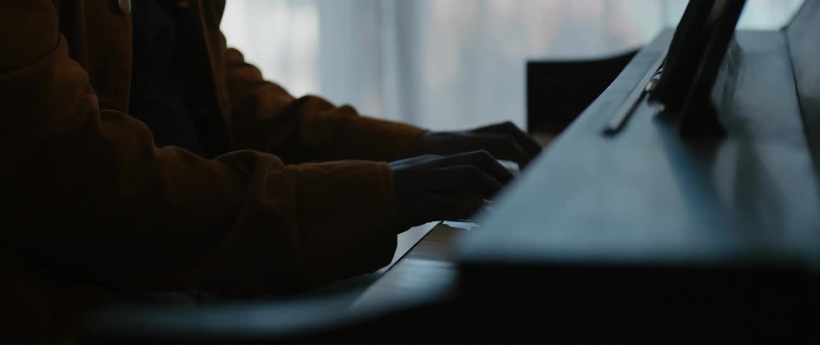 A man is sitting indoors and playing the piano instrument