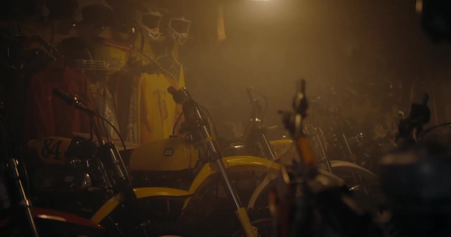 Motocross dirt bikes helmets and gear in a dim lit shop