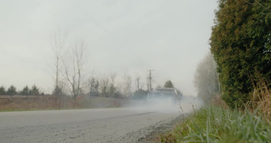 A car is driving down the road in the middle of the day