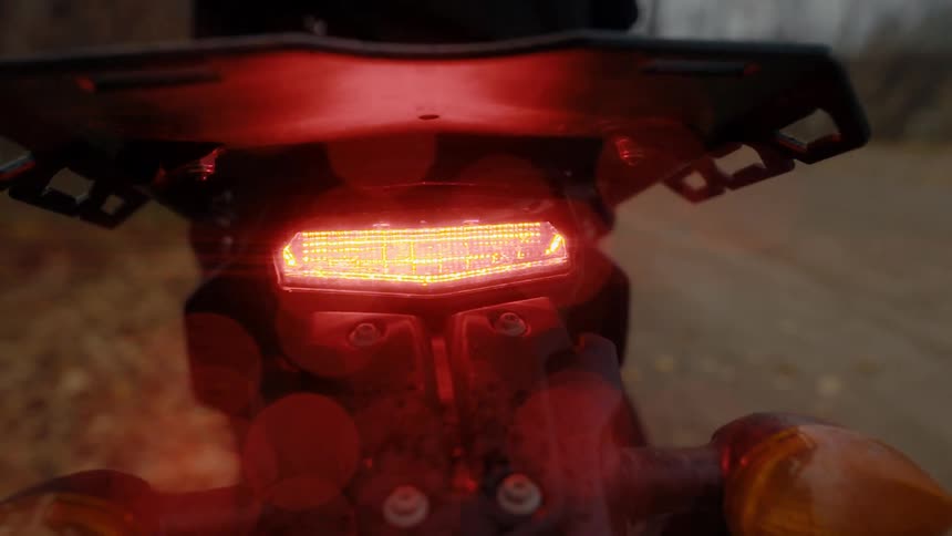 Motorcycle red light blinks on bike parked near side of road strewn with fallen leaves