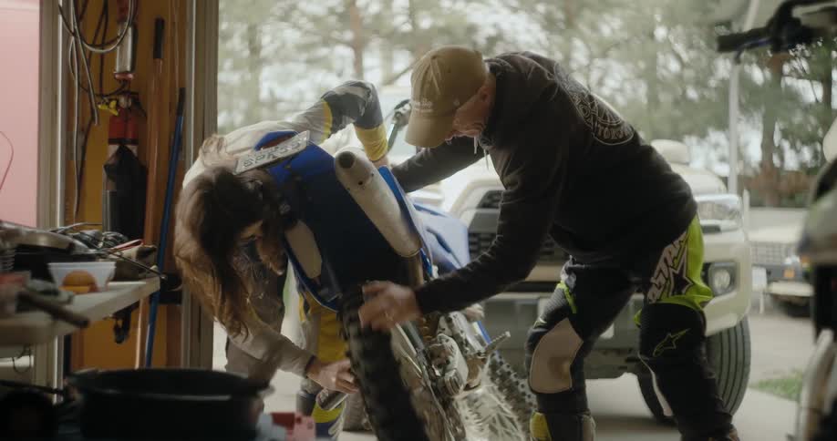 Two men work on a dirt bike in the garage