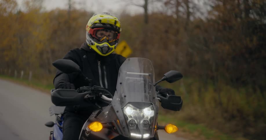 Man wearing a yellow crash helmet rides a motorcycle on a road