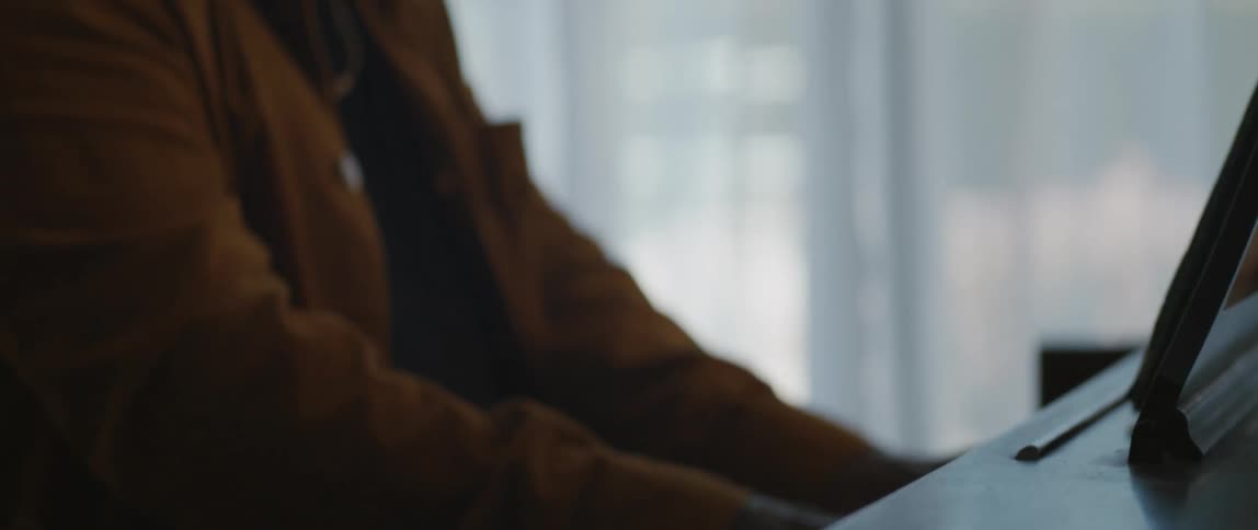 Male musician with black cap and orange jacket plays piano in room
