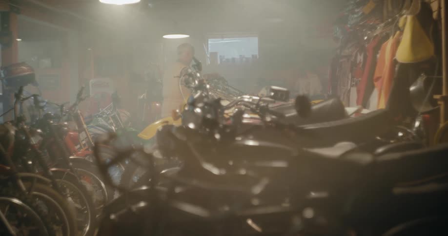 A man walks through a smoky room full of motorcycles