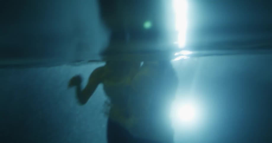 A man and woman have jumped into a pool with their clothes on and are splashing and playing