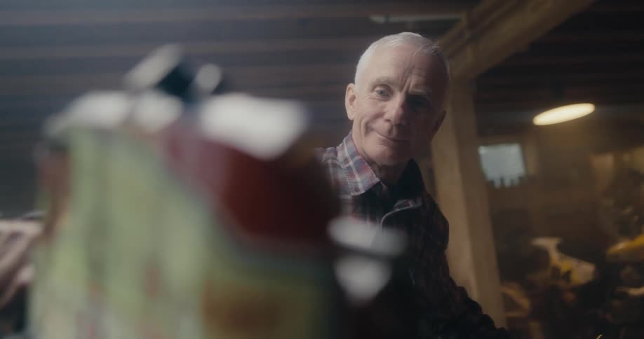 An elderly man in a plaid shirt smiling while looking at something in a basement