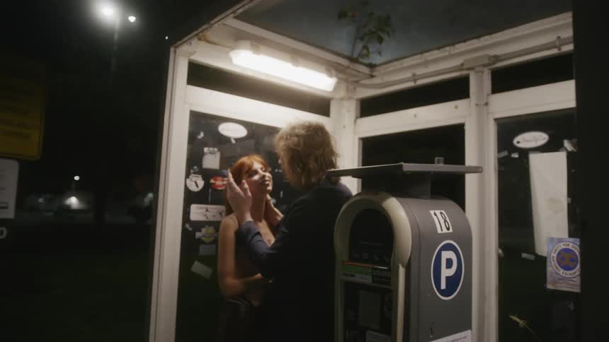 A man tosses his cigarette to start kissing his girlfriend in a bus shelter