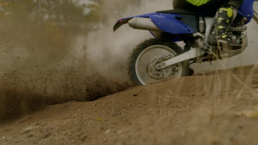 Smoke and dirt fly as a cyclist rides a motorbike on a trail in the woods