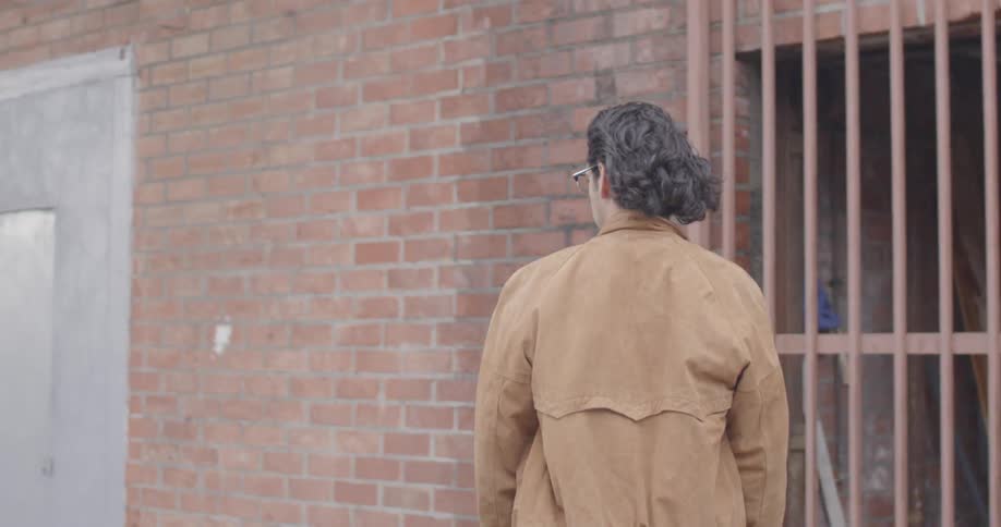 A man in a brown jacket skateboards past a building