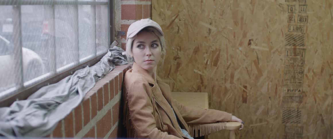 A young woman sits on a chair against a brick wall