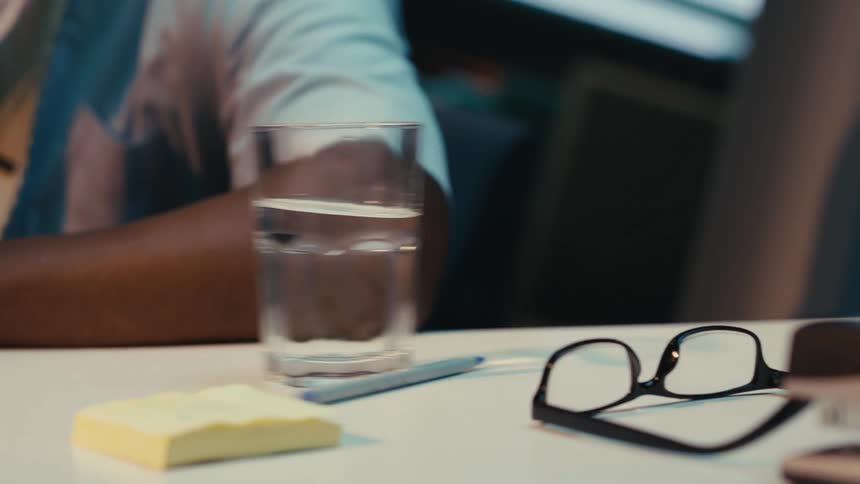 A conference table tilts causing everything to slide off while a man sits with elbow on the table