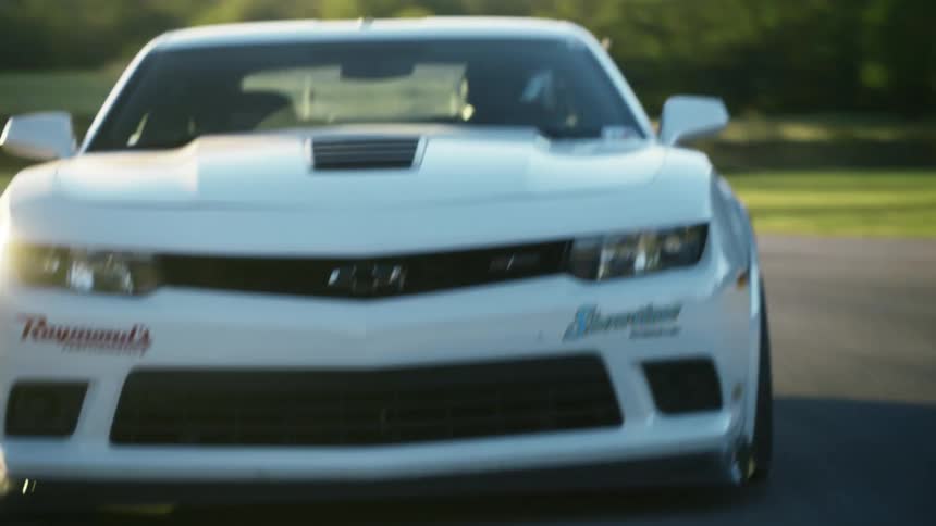 The sun shines brightly as a white automobile travels fast on a road
