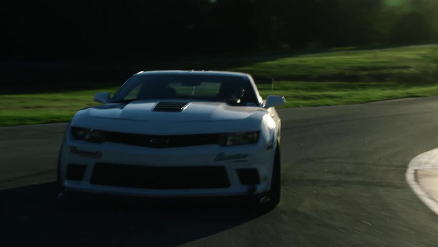 The sun shines brightly as a white automobile travels around a curve