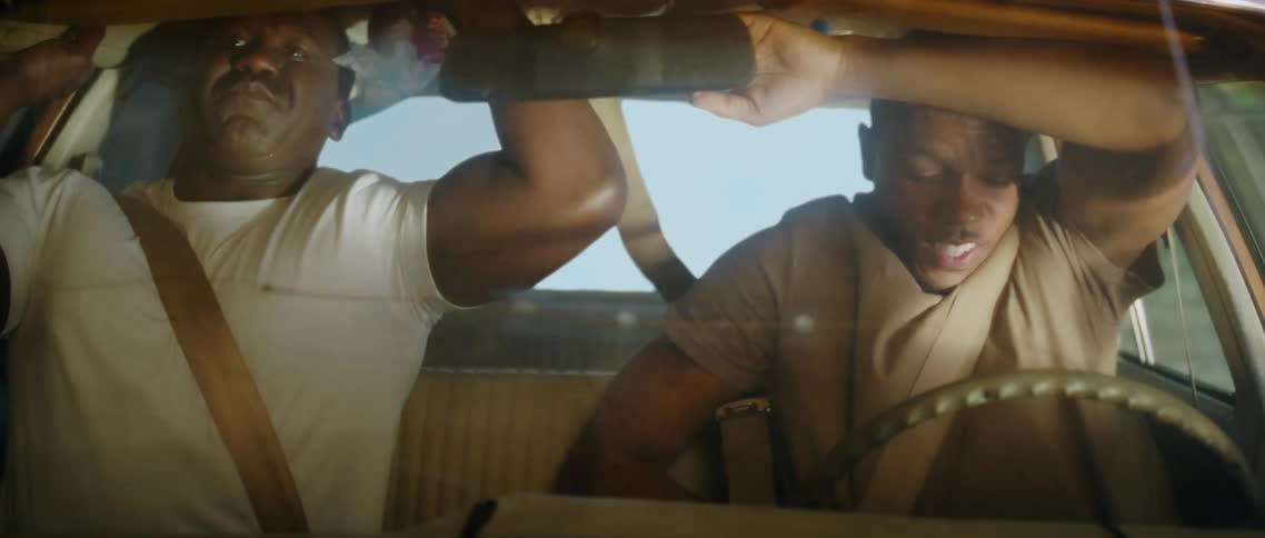 Two men are in a vehicle together and look frightened